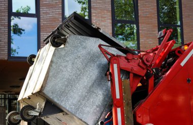 VENLO, NEtherlands - 8 AĞUSTOS. 2019: Hidrolik kollarıyla ağır bir çöp konteynırını kaldıran kırmızı çöp kamyonuna bakın