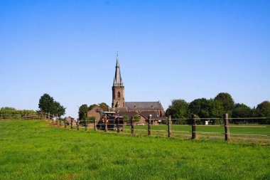 Kırsal kesimdeki ıssız neo-gotik kilisedeki çitli yeşil tarlalara bakın - Viersen Dornbusch, Almanya