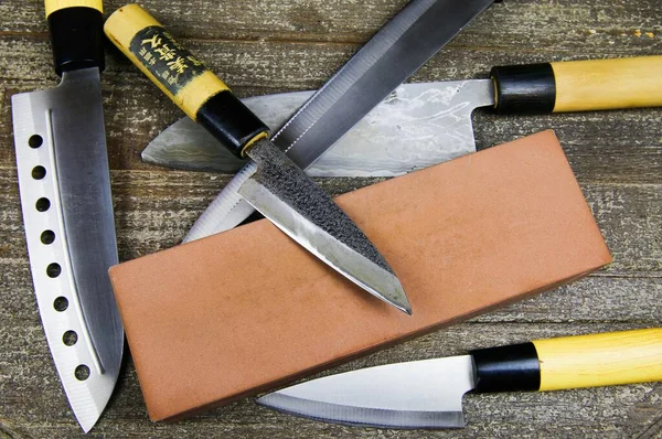 Öğütücü bıçaklar: Ahşap masa üzerinde bileme taşı olan farklı metal Japon mutfak bıçaklarını kapatın