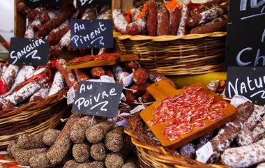 Fransız salamlarının farklı türleri hasır sepetlerde, çiftçi pazarında elle yazılmış tebeşir tahtalarıyla sunuluyor - St. Tropez, Fransa