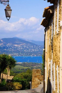Eski evlerin ve sokak lambalarının ötesini görmek için Akdeniz 'in tepesindeki Gassin köyünden St. Tropez körfezinin mavi denizine bakın. St. Maxime arka planında bulanık dağ.