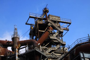 Landschaftspark Duisburg, Almanya: Paslı boru hattıyla paslanmış kulede derin mavi gökyüzüne açılan merdivenler alçak açılı görünüyor