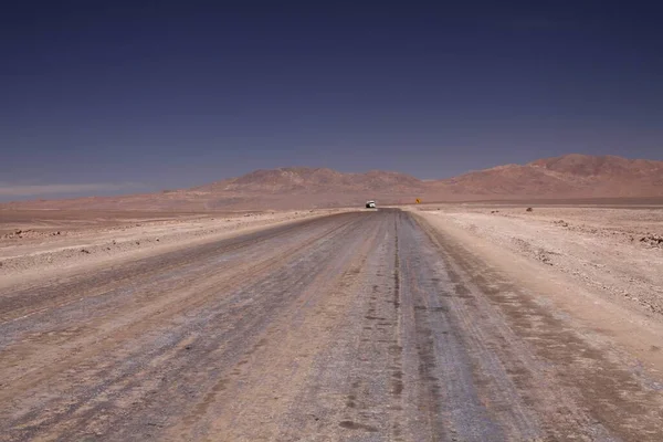 无边无际的土路通向无边无际的盐滩高原 与蔚蓝无云的天空形成鲜明对比 地平线上孤立的卡车和黄色的交通标志 指示着向左的方向 智利阿塔卡马沙漠 — 图库照片