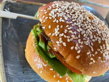 Susamlı, yeşil salatalı, soğanlı ve domatesli sulu sığır burger.