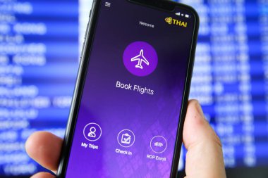 Viersen, Almanya - 6 Temmuz. 2020: Tay Havayolları uçuş rezervasyon uygulaması ile cep telefonunun kapatılması. Bulanık çıkış tahtası arka planı. (Kitap uçuşlarına odaklan)