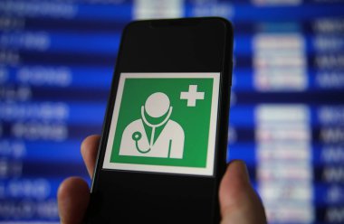 Viersen, Almanya - 9 Temmuz. 2020: Havaalanında sağlık ve tıbbi yardım için yeşil işaretli cep telefonu görüntüsü. Bulanık çıkış tahtası arkaplanı.