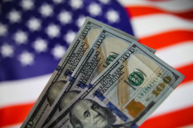 Üç tane 100 dolarlık banknot tutan münferit ele bakın. Bulanık ABD bayrağı geçmişi. (