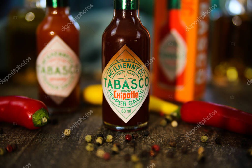 Viersen, Germany - July 9. 2020: Closeup of Tabasco hot chipotle pepper sauce on wood table with peppercorns and chillis
