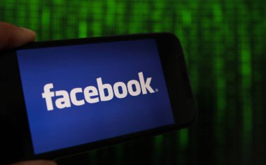 Viersen, Almanya - 9 Temmuz. 2020: Facebook logosu elle tutulan cep telefonundan görüntüle. İkili kod numaralarının geçtiği bir ekran.