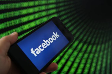Viersen, Almanya - 9 Temmuz. 2020: Facebook logosu elle tutulan cep telefonundan görüntüle. İkili kod numaralarının geçtiği bir ekran.