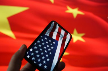 Çin Amerika 'nın ekonomik ilişki konsepti: ABD bayrağıyla el ele tutuşan cep telefonuna bakın. Çin arkaplanının bulanık bayrağı. (üst sıradaki yıldızlara seçici odak)