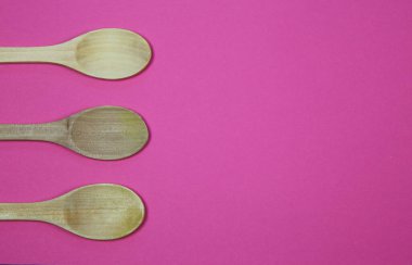 Pembe arkaplanda üç tahta kaşıkta yüksek açı görünümü ve metin için boş kopya alanı