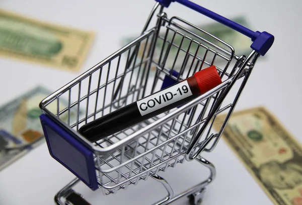 View on modell of shopping cart with covid-19 blood sample tube and us dollar bills background  -consumer behaviour and retail  trade during corona crisis concept