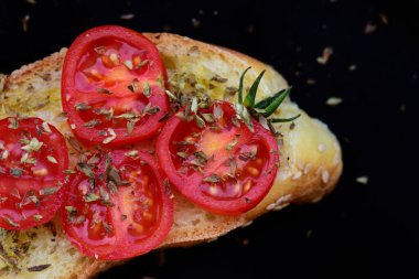 Bir dilim yeşil zeytinyağlı İtalyan beyaz ekmeği ve koyu arkaplanda kekik soslu domates dilimleri.