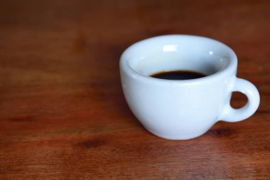 Espresso için beyaz eski bir fincan, ahşap bir masanın üzerinde kahve duruyor.