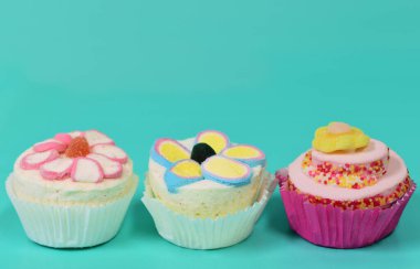 Köpük şekerden yapılmış üç renkli bardak. Davetiye için bolca yeri olan yeşil bir zemine karşı yan yana durun.