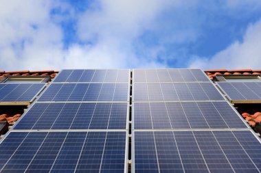 Kırmızı çatı kiremitleri olan bir aile evinin çatısındaki güneş panelinin arka planı ve yakın plan görüntüsü bulutlu mavi gökyüzüne ve güneş ışığından gelen enerji için güneşe karşı.