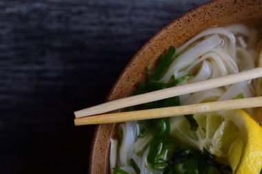 Vietnam eriştesi ve limonlu sebze çorbası, bir pho, üzerinde bambu çubukları olan kahverengi bir kâse ve metin için yer.