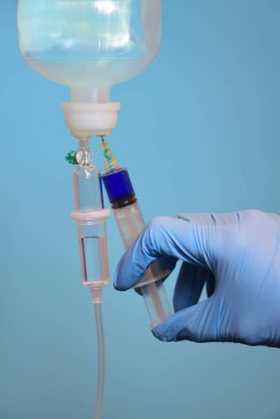 Mavi el ayakkabılı bir el şırıngası enjekte edilmiş mavi bir ilaç, dikey arkaplanda hafif bir arkaplana karşı bir infüzyon içine