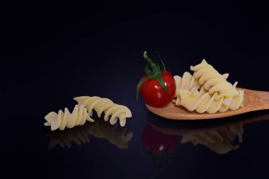 Tahta bir kaşıkta sarmal makarna ile domatesli koyu arkaplanı yakın plan.