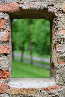Eski bir tarihi taş duvar doğaya bakan bir açıklığın etrafında bir çerçeve oluşturur.