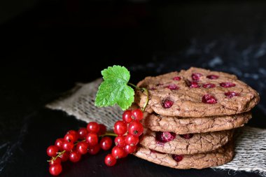 Frenk üzümlü çikolatalı bisküviler mermerin üstünde ve koyu bir zemin üzerinde taze böğürtlenlerle istiflenir.