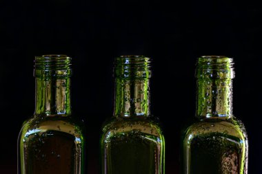Üç yeşil cam şişe ve su damlaları koyu bir arka planda yan yana duruyor.