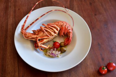 Kaynamış bir ıstakoz beyaz bir tabakta yatıyor ve arka plan olarak ahşap bir masada.