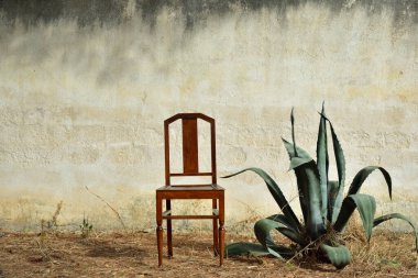 Eski bir kırsal duvarın arkaplan görüntüsü açık havada, önünde eski bir sandalye duruyor Kuru toprakta yazın bir agave yanında.