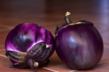 Sicilya 'da yaz aylarında koyu arkaplan önünde kahverengi fayansların üzerine iki leylak yuvarlak patlıcan uzanır.