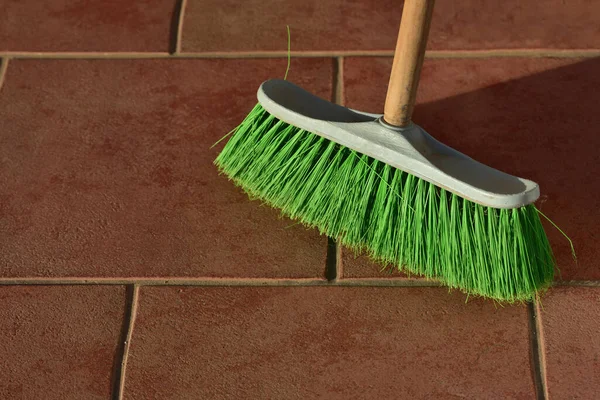 A green used broom with bristles cleans the floor on brown tiles as background