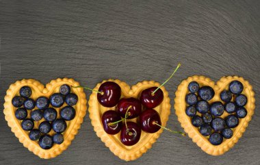 Yaban mersini ya da kirazlı üç kek siyah bir tabakta duruyor.