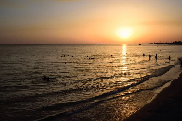 Akşamları gün batımında, birçok insan denizde ve kırmızı ve parlak bir arka planda banyo yapıyor.