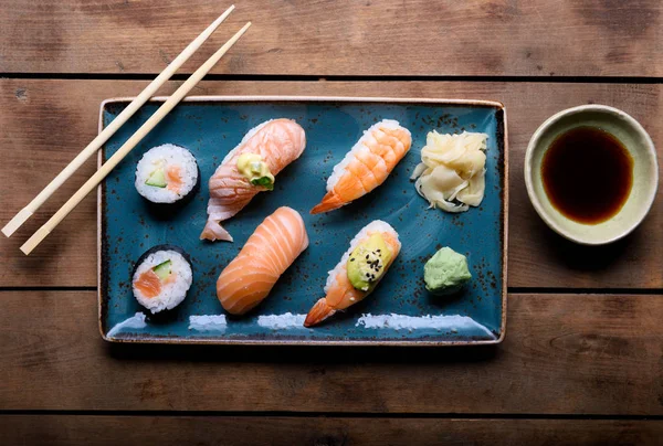 Blue plate with selection of sushi, chopsticks and soy sauce on a vintage wooden chest