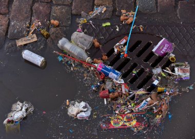 Helsinki, Finlandiya - 1 Mayıs 2017: Mayıs kutlamalarının ilkinden sonra, kanalizasyon üzerinde ve kısmen Arnavut kaldırımlı sokakta ki bir su birikintisinde yüzen plastik ve diğer çöpler. 