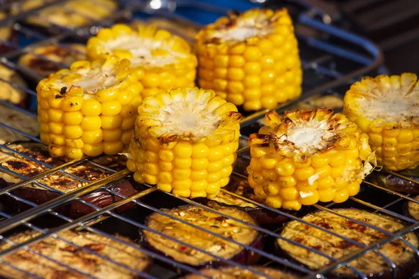 Cooking several fresh yellow brown golden corn cobs on open air barbecue grill, close up.