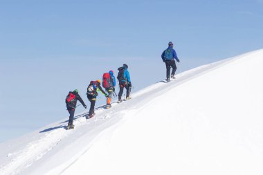 Bir grup dağcı karla kaplı bir dağ tepesine tırmanıyor