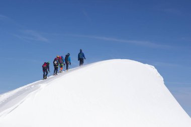 Bir grup dağcı karla kaplı bir dağ tepesine tırmanıyor