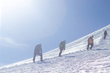Bir grup dağcı karla kaplı bir dağ tepesine tırmanıyor