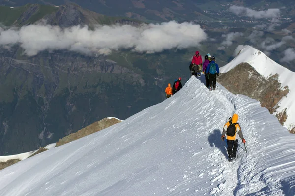 En grupp bergsklättrare klättrar till toppen av ett snöklädda berg — Stockfoto