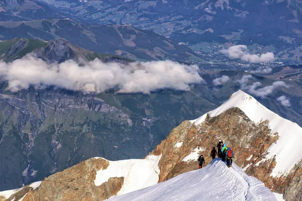 A group of mountaineers climbs to the top of a snow-capped mountain.