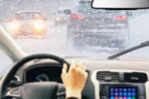 バック グラウンドで雪に覆われた車とストレートの氷の道路の明るい雪の降る冬の日中ドライバー ステアリング ホイールに手をインテリアの一部と車の中からの眺め — ストック写真