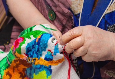 Yaşlı bir kadın parmakları embroiders. Yukarı clouse