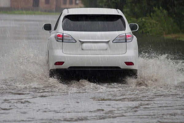 Червоний автомобіль їде у сильний дощ на затопленій дорозі — стокове фото