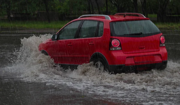 Carro vermelho monta em chuva pesada em uma estrada inundada — Fotografia de Stock