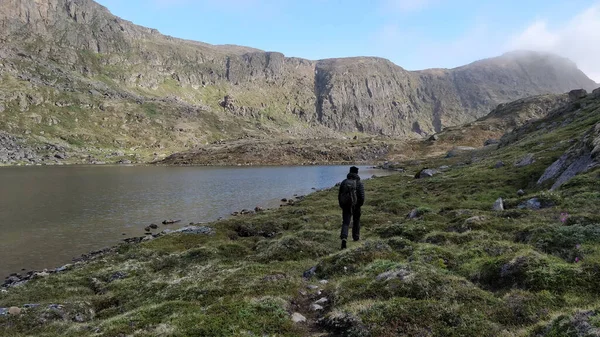 Genç bir adam Grönland 'daki Sisimiut civarındaki dağlarda bir gölün yanında yürüyüş yapıyor.
