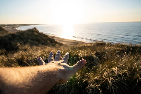 Bir el, güneşin okyanusun üzerinde batmakta olduğu Danimarka 'nın kuzey kesiminde güzel bir günbatımına uzanıyor.