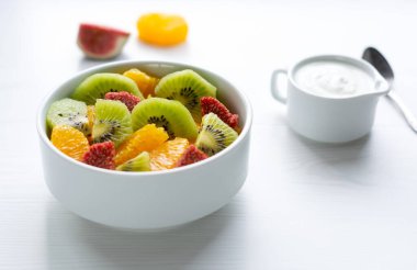 Kivi, portakal ve incir salatası beyaz bir salata kasesinde ışık masasında yatıyor.