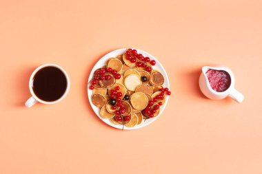 Şeftali arka planında kırmızı ve siyah üzümlü beyaz bir tabakta lezzetli mini poşetler, bir fincan espresso ve kırmızı frenk üzümü reçelinin yanında, düz yatak, lezzetli bir kahvaltı kavramı..