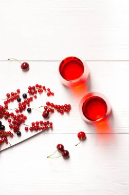 Kırmızı üzümlü, kirazlı, siyah üzümlü iki bardak beyaz ahşap arka planda duruyor. Yanlarında böğürtlen, üst manzara..